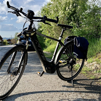 Ein E-Bike mit Satteltaschen, im Hintergrund ein Auto und eine Wohnstraße
