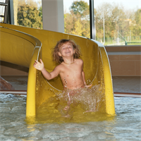 Ein Kind rutscht auf einer gelben Wasserrutsche in ein Schwimmbecken